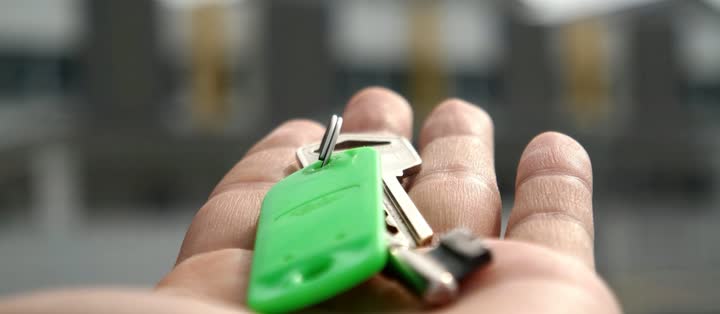 Hand holding house keys outside a home