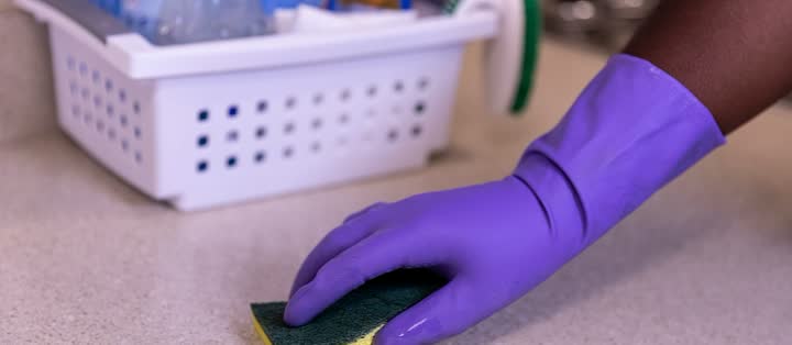 Gloved hand wiping a kitchen counter with a sponge